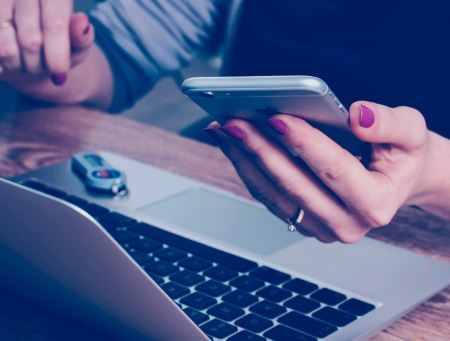 Image of a woman's hand holding a phone in front of a laptop