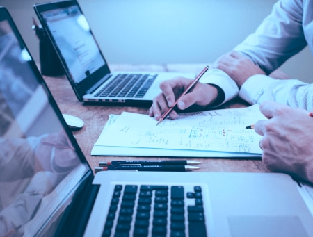 image of two people in fron of their laptops discussing something written on the paper